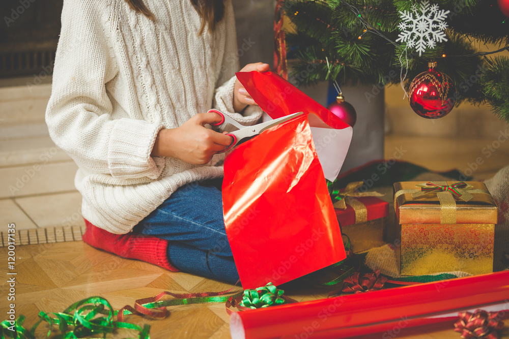 Fototapeta premium Closeup of girl sitting under Christmas tree and cutting red pap