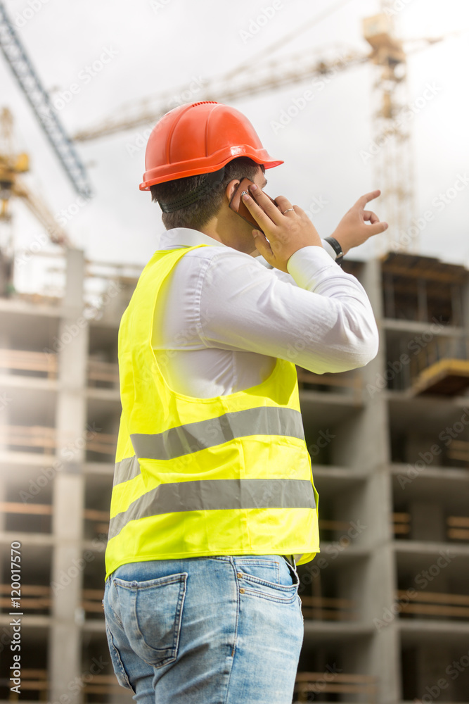 Engineer in hardhat talking by phone and pointing at building si Engineer in hardhat talking by phone and pointing at building si