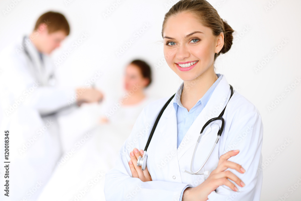 Cheerful smiling female doctor on the background with physician and his patient in the bed. High level and quality of medical service concept. Cheerful smiling female doctor on the background with physician and his patient in the bed. High level and quality of medical service concept.