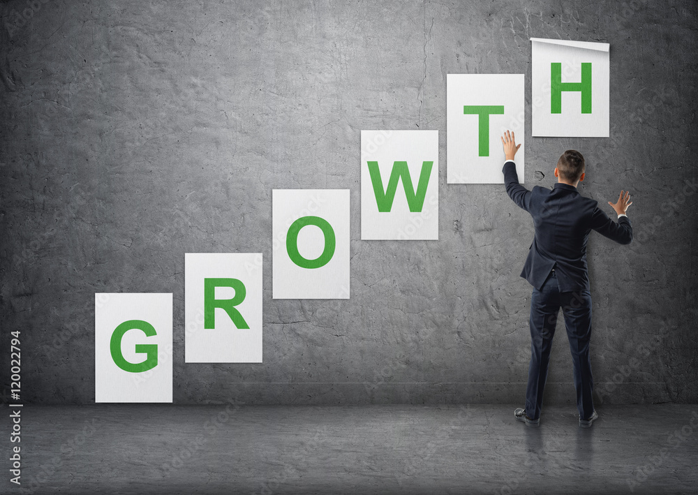 Businessman putting up posters with letters on concrete wall that form 'growth' word Businessman putting up posters with letters on concrete wall that form 'growth' word