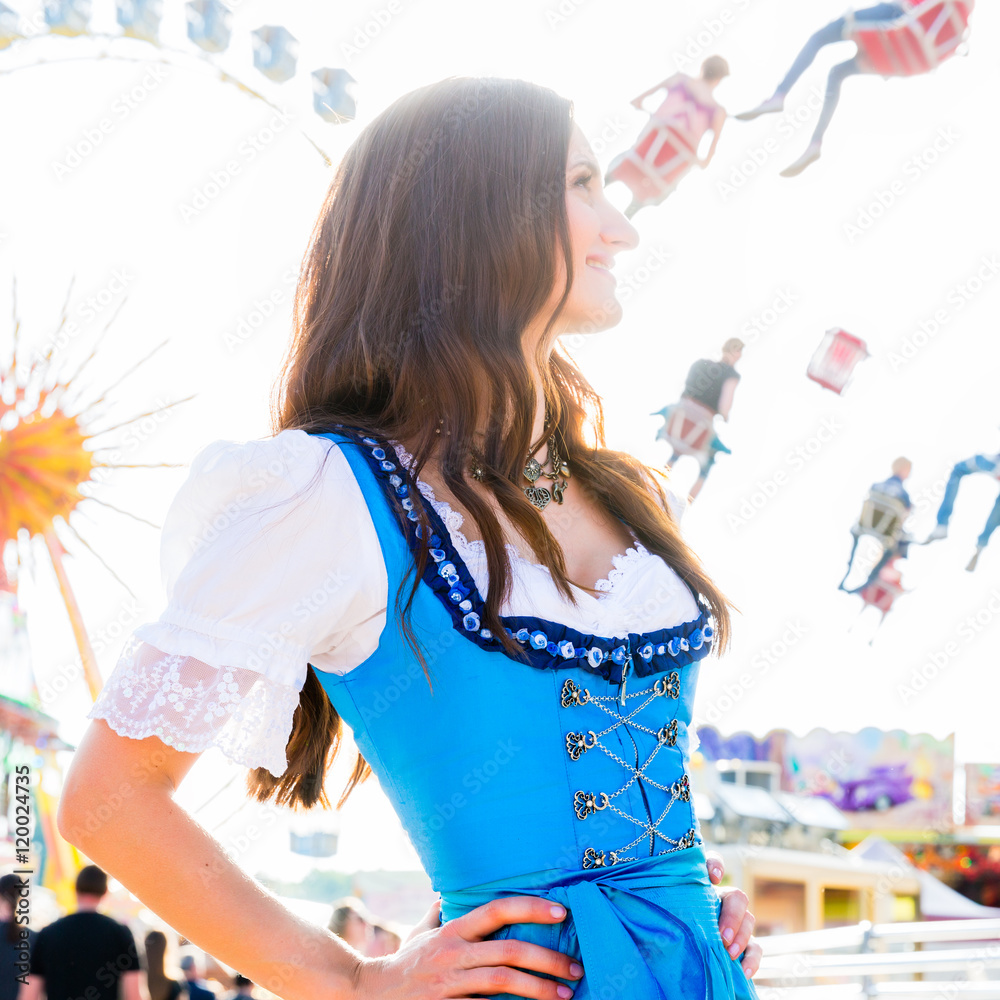 Frau im Dirndl steht lächelnd vor Riesenrad und dem Kettenkarussell auf bayrischem Volksfest - obrazy, fototapety, plakaty 