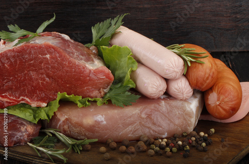 meat and sausages with vegetables and spices on wooden background