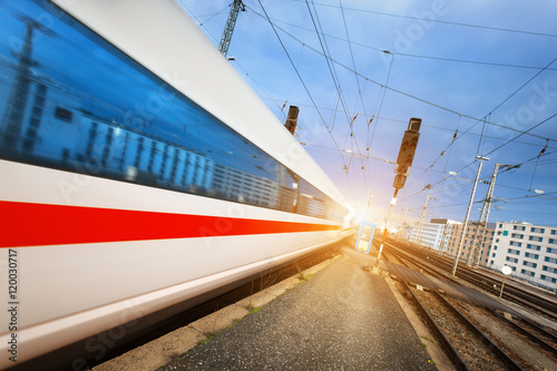 High speed white passenger train on tracks in motion at sunset. Commuter train. Railway station. Railroad with vintage toning. Travel background. Train