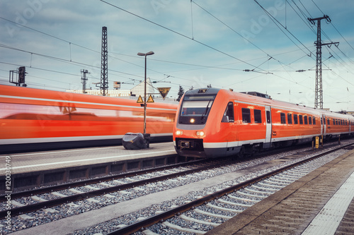 Fotografie Modern high speed red passenger commuter trains at the railway platform at sunset with vintage toning
