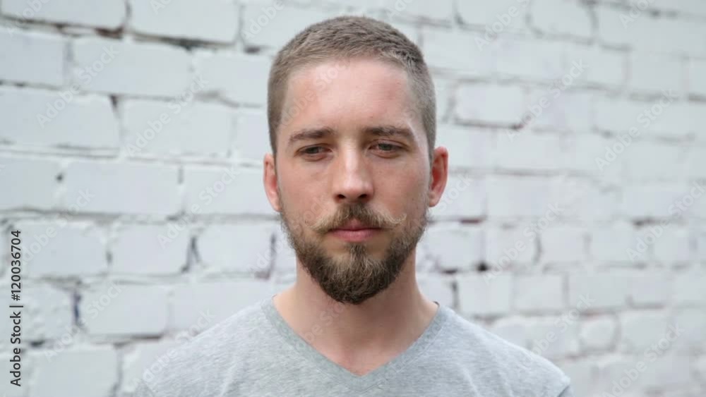 Young serious man looks away, white brick wall background Young serious man looks away, white brick wall background