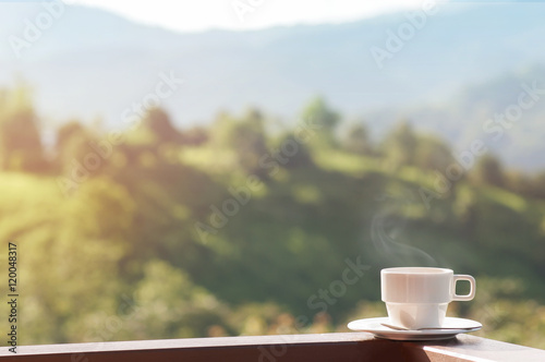 White cup of hot coffee on balcony with natural and mountains.