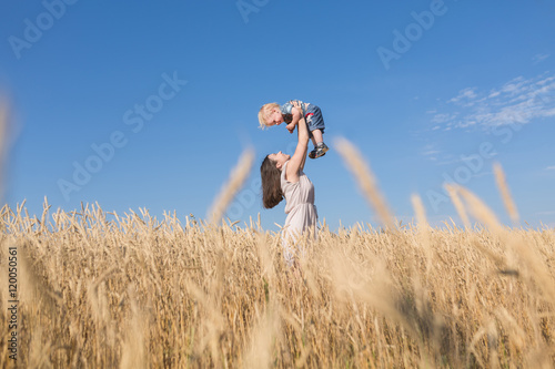 Portrait of young mother and her one year old baby boy in a wheat gold field with blue sky. Happe family beautiful concept