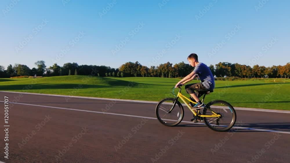 Steadicam shot: The teenager goes on a flat road on a background of a green golf course Steadicam shot: The teenager goes on a flat road on a background of a green golf course