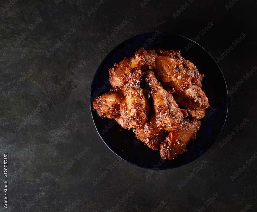Fried chicken wings on rustic serving board, spicy tomato sauce, herbs and mug of light beer over black wooden backdrop, top view