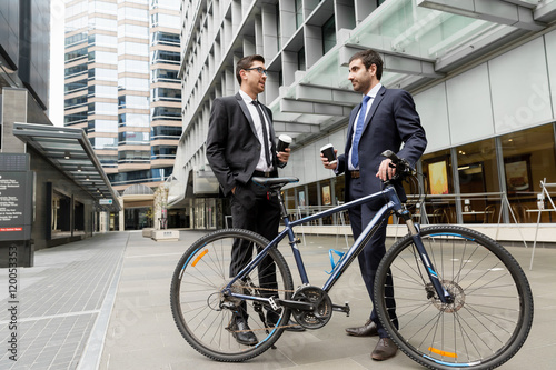 Two young businessmen with a bike in city centre