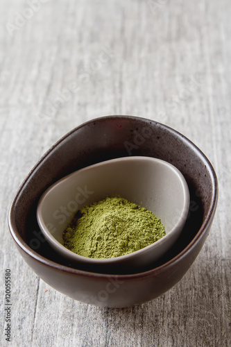 Dry Matcha tea in a small brown plate. Grey wood background