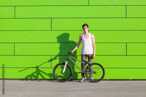 Boy with silver bike stay at green wall background