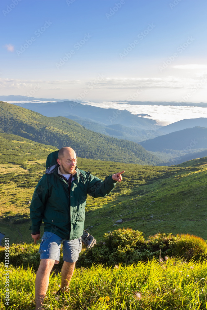 Young man standing on the top of mountain and show finger at far away in sunrise time, Carpathians.