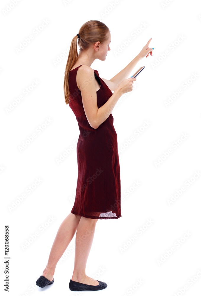 back view of pointing young beautiful woman and using a mobile phone. Isolated over white background. Slim blonde in a burgundy dress that tells the reading from the tablet. back view of pointing young beautiful woman and using a mobile phone. Isolated over white background. Slim blonde in a burgundy dress that tells the reading from the tablet.