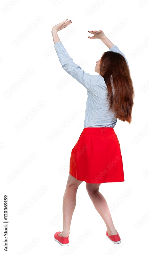 back view of woman protects hands from what is falling from above. Long-haired brunette in red skirt protects hands from above. back view of woman protects hands from what is falling from above. Long-haired brunette in red skirt protects hands from above.