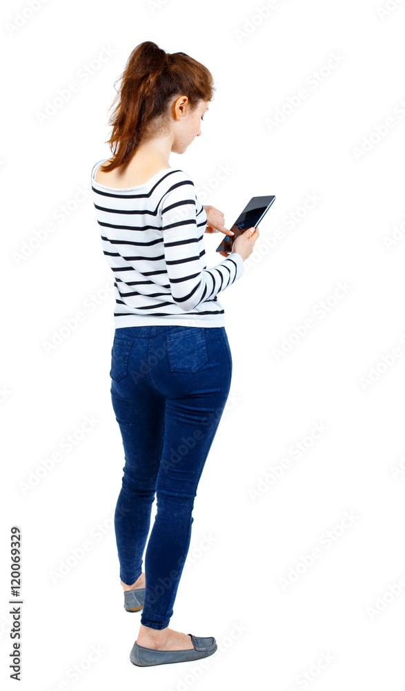 back view of standing young beautiful woman using a mobile phone or tablet computer. Girl in a striped sweater drives a finger on the tablet. back view of standing young beautiful woman using a mobile phone or tablet computer. Girl in a striped sweater drives a finger on the tablet.
