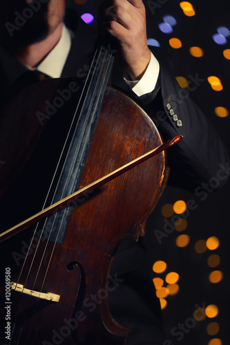 Man playing cello in darkness on blurred lights background