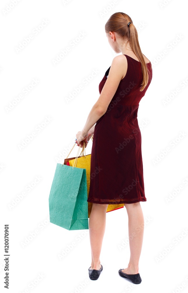 back view of woman with shopping bags. Isolated over white background. Slim blonde in a burgundy dress holding colorful bags in hand. back view of woman with shopping bags. Isolated over white background. Slim blonde in a burgundy dress holding colorful bags in hand.