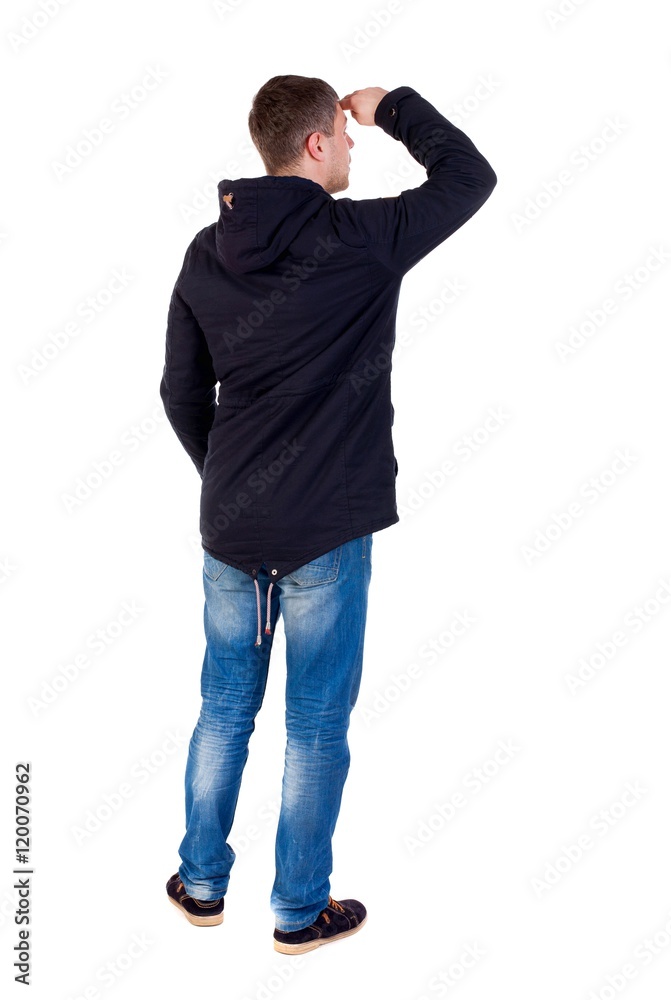 Back view of handsome man in winter jacket looking up. Standing young guy in parka. A guy in a black jacket looks afar having put his hand to his eyes. Back view of handsome man in winter jacket looking up. Standing young guy in parka. A guy in a black jacket looks afar having put his hand to his eyes.