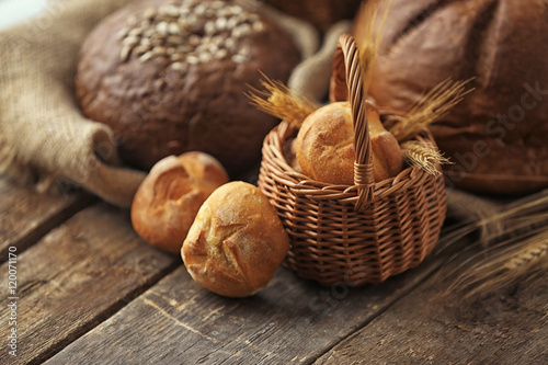 Basket with bread buns and spikes of wheat on a wooden table