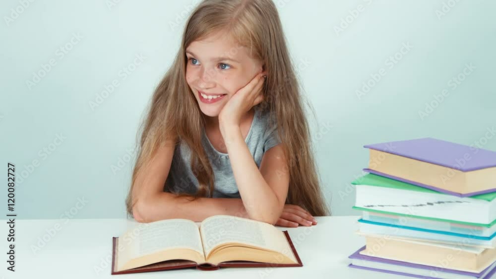 Close up portrait happy girl 7-8 years old reading book on the table and smiling away with teeth on white background Close up portrait happy girl 7-8 years old reading book on the table and smiling away with teeth on white background