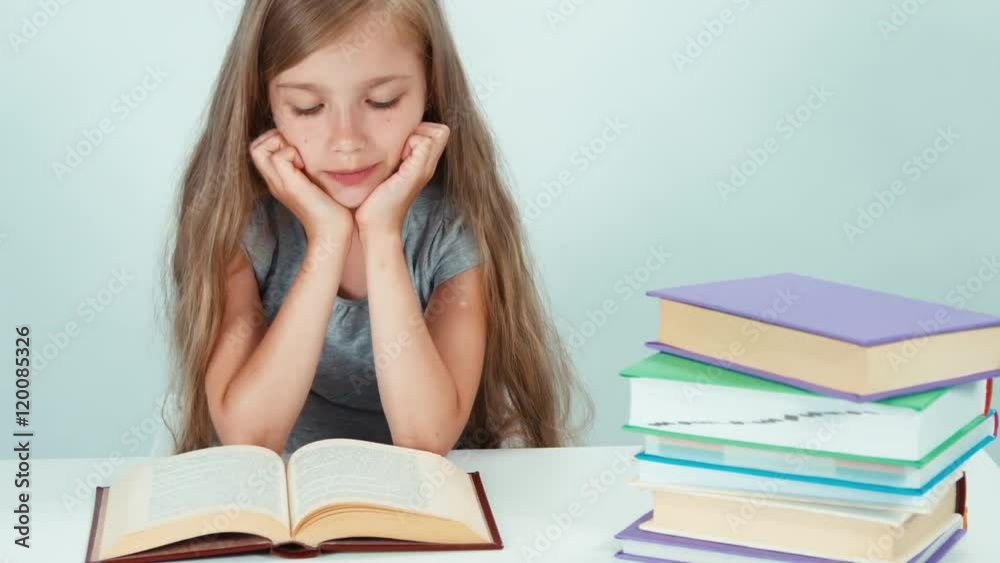 Close up portrait happy schoolgirl 7-8 years old reading book on the table and looking at camera on white background Close up portrait happy schoolgirl 7-8 years old reading book on the table and looking at camera on white background