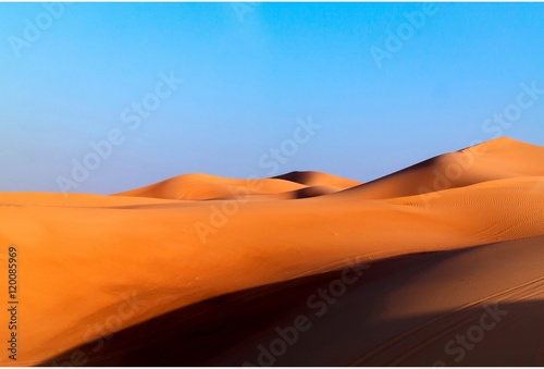 Fototapeta Naklejka Na Ścianę i Meble -  Arabian desert dune background on blue sky. Desert near the city of Dubai. large red and yellow dune illuminated by bright sunlight