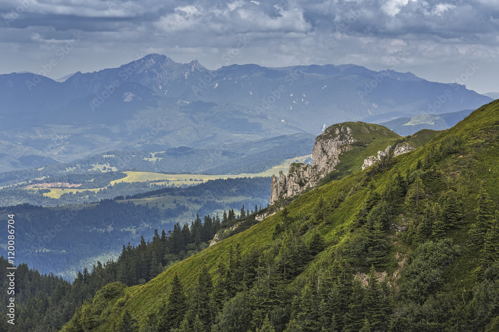 Scenic alpine landscape with green slope and Ciucas Mountain range at  the horizon as seen from Piatra Mare Massif, Romania.