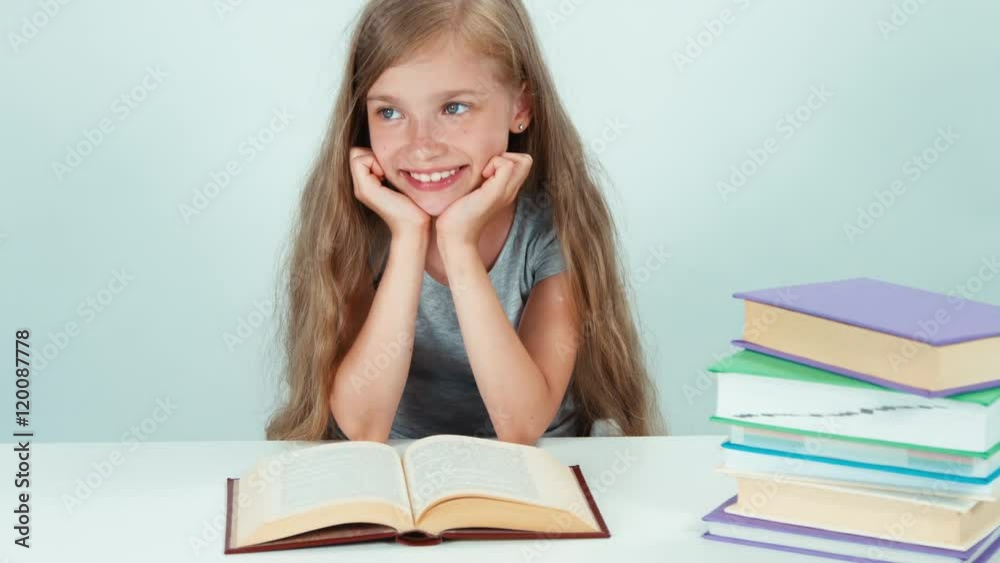 Close up portrait happy schoolgirl 7-8 years old reading book on the table on white background Close up portrait happy schoolgirl 7-8 years old reading book on the table on white background