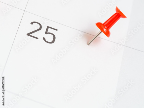Red pin pinned on the 25th date of the month on calendar paper