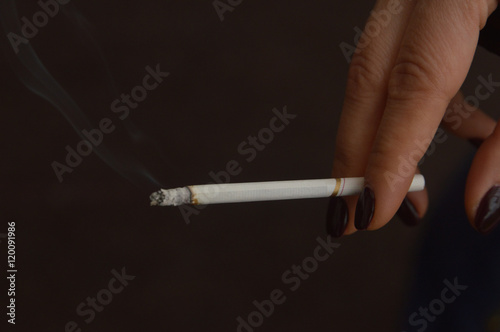 Woman's hand with dark polished nails holding a lit cigarette