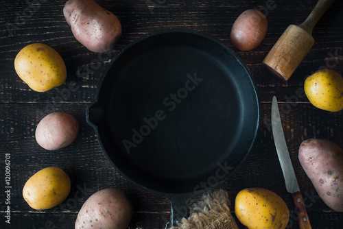 Cooking pan surrounded by raw potatoes on the wooden table top view