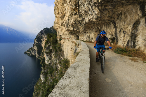 Mountain biking at sunrise man over Lake Garda on path Sentiero della Ponale, Riva del Garda, Italy