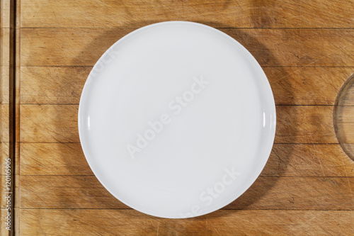 Flat white shallow porcelain plate on wooden cutting board directly from above