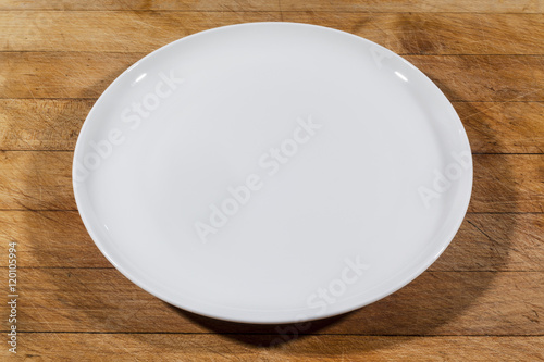 Flat white shallow porcelain plate on wooden cutting board from side