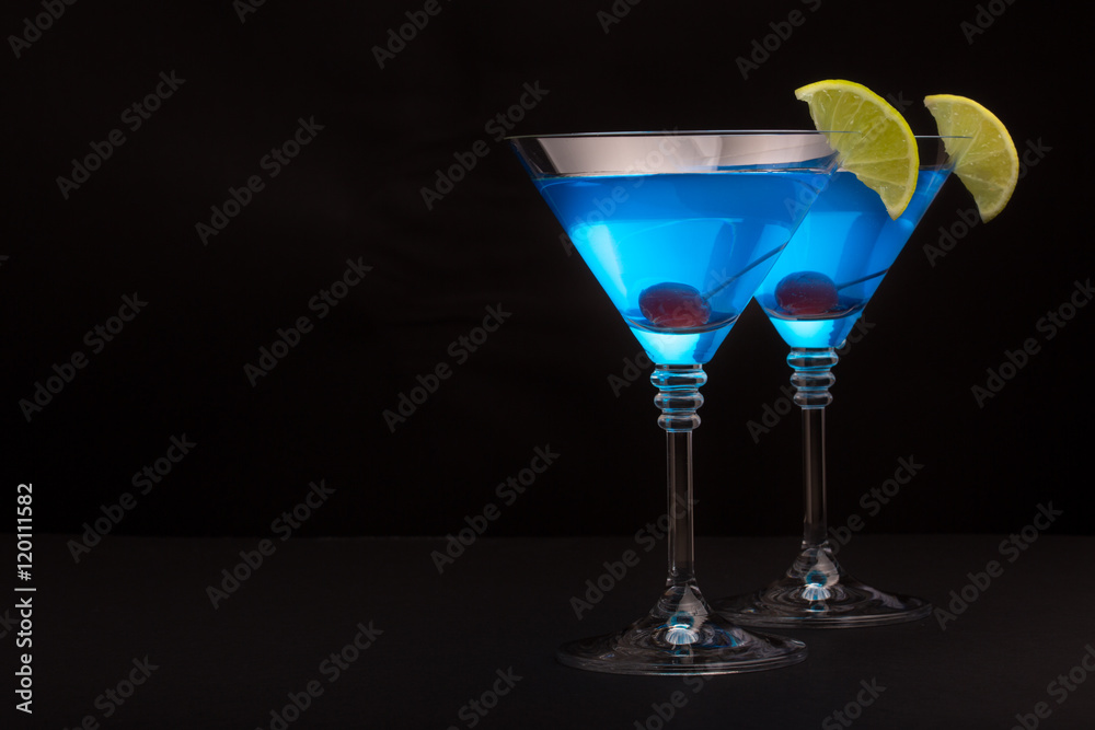 Blue curacao cocktail with lime and cherry in martini glasses on black background