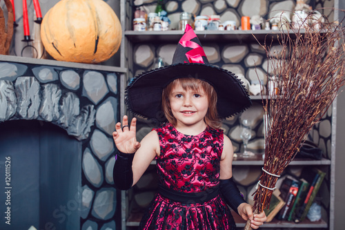 Girl in witch costume standing in halloween decorations with a broom in his hand