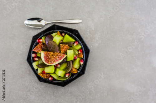 Delicious and healthy fresh fruit salad with figs, melon and pomegranate in bowl. Vegetarian food on grey stone background.