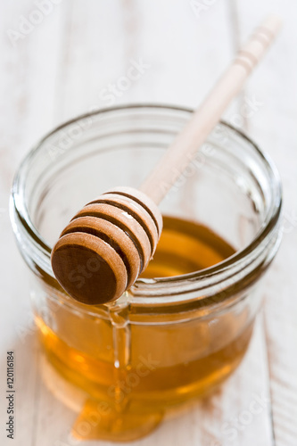 Honey dipper with honey in a jar on white wooden table

