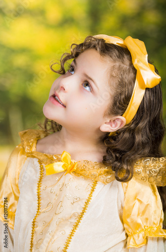 Cute little girl wearing beautiful yellow dress with matching head band, posing for camera, green forest background