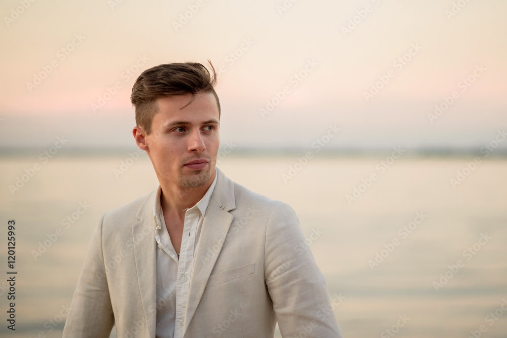 young handsome man in a white suit near the sea at sunset. young handsome groom on the beach. Close-up