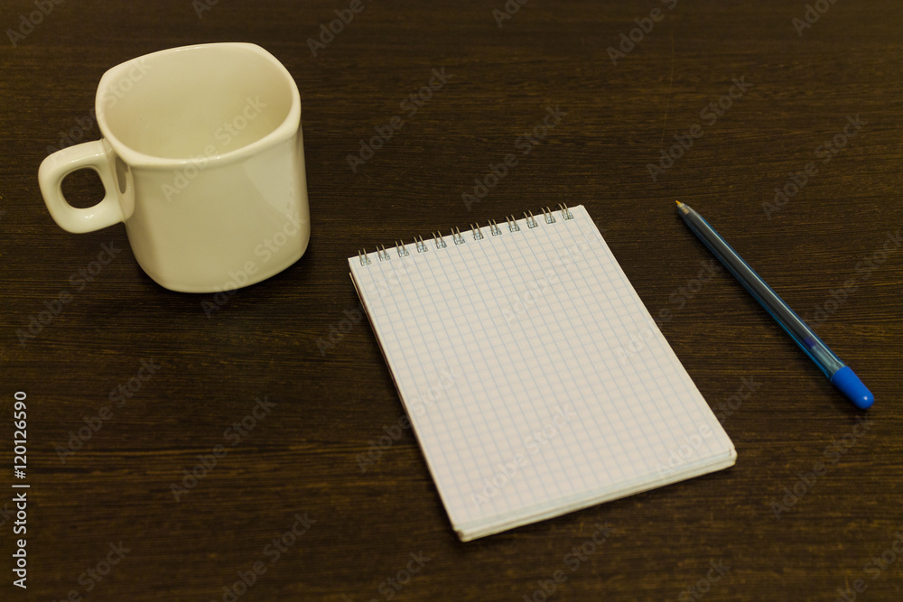 White notepad with a pen on a brown table with a cup of coffee White notepad with a pen on a brown table with a cup of coffee