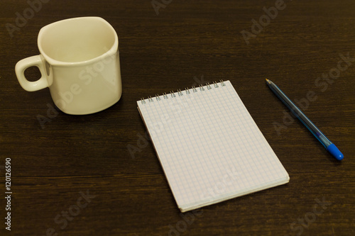 White notepad with a pen on a brown table with a cup of coffee