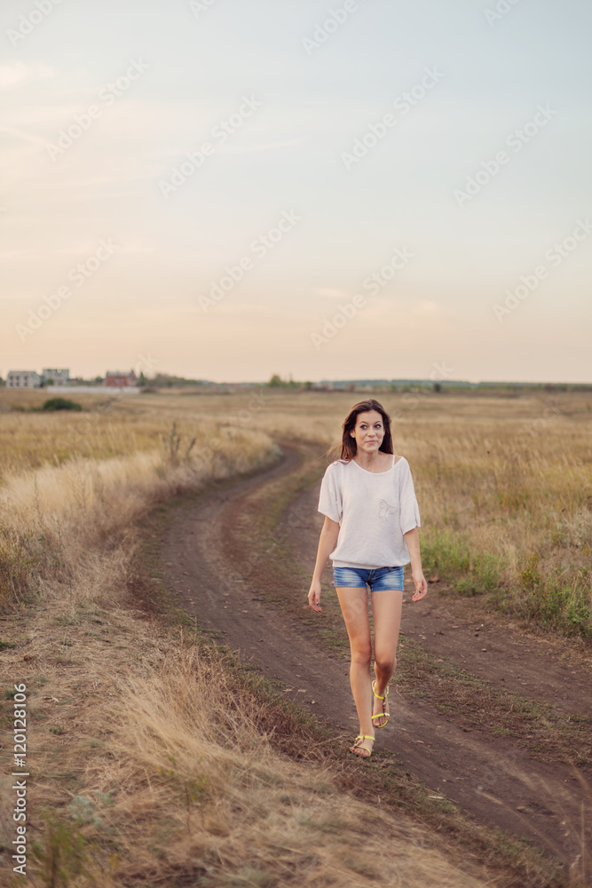 Young girl with long brown hair walking along the road in field