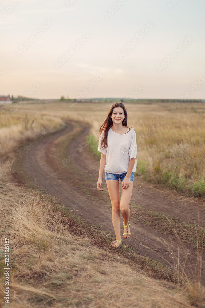 Young girl with long brown hair walking along the road in field Young girl with long brown hair walking along the road in field