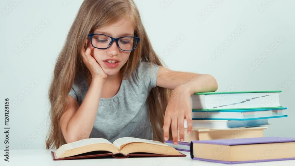 Portrait cute student girl with long blond hair 7-8 years in glasses reading book and looking away Portrait cute student girl with long blond hair 7-8 years in glasses reading book and looking away