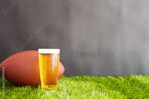 Vintage football and beer glass over grass and black background
