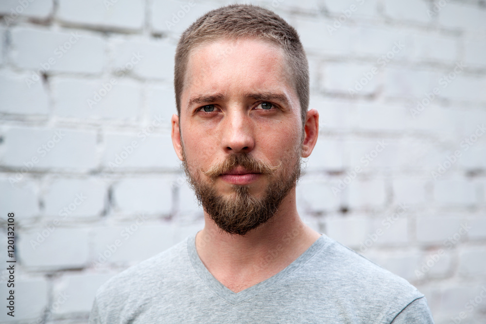 Serious man with a beard and mustache looking at the camera, white brick wall background Serious man with a beard and mustache looking at the camera, white brick wall background
