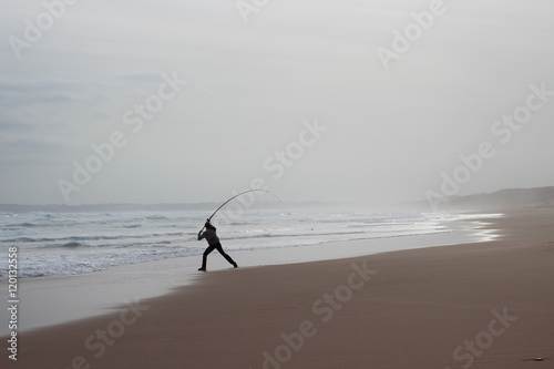 Fisherman mid-cast on beach