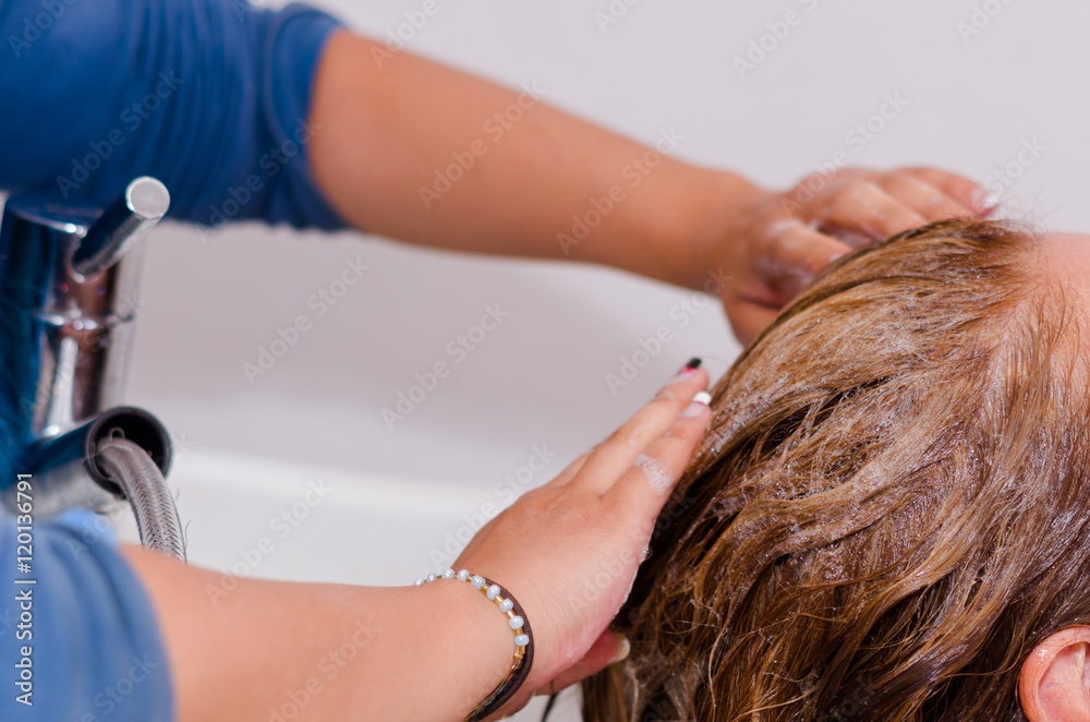 Fototapeta premium Hands washing with shampoo a long dyeing hair, inside a hairdressing saloon